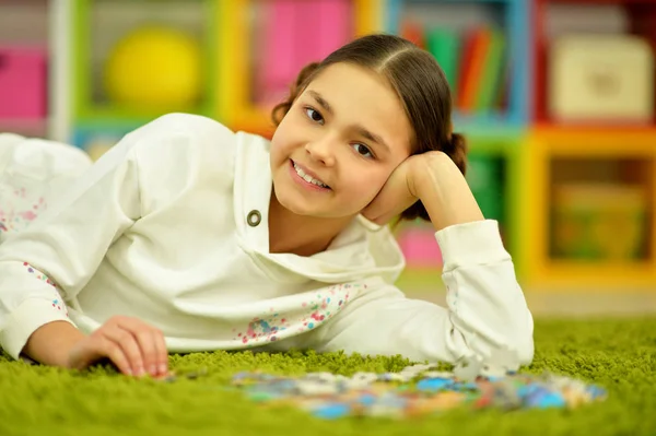 Cute Little Girl Collecting Puzzle Pieces While Lying Green Carpet — Stock Photo, Image