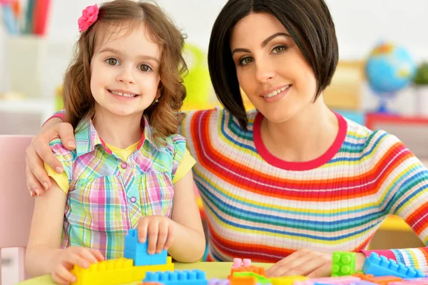 かわいい女の子と彼女の母親が彼女の部屋でカラフルなプラスチック製のブロックを一緒に遊んで — ストック写真
