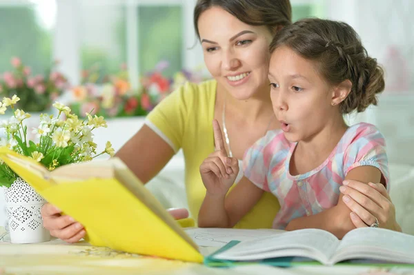 Klein Schattig Meisje Lezen Boek Met Moeder Aan Tafel Thuis — Stockfoto