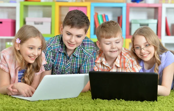 一群孩子躺在地板上 铺着绿色的地毯 看着现代的笔记本电脑 — 图库照片