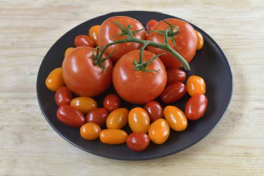 Doğal ahşap masada izole siyah tabak üzerinde küçük kiraz domates ile Taze dört olgun domates