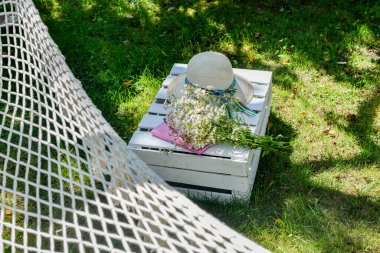 Hammock in the garden, relax. Book, wildflowers and summer hat ona a white crate