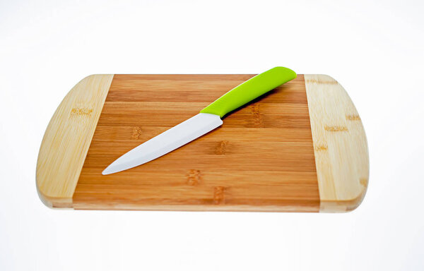 Chopping board made of beech wood with a ceramic knife with a green handle lying on it.