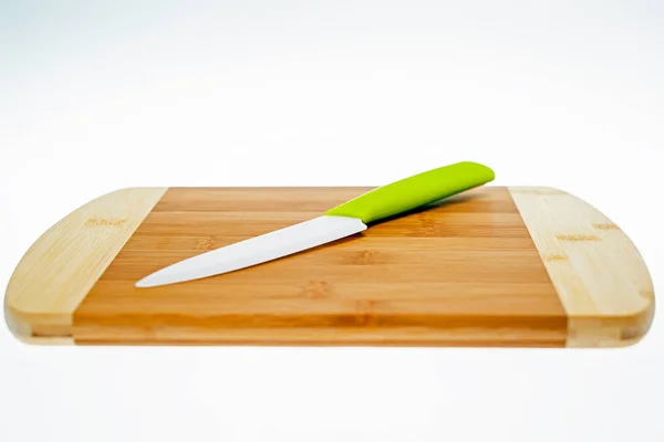 Chopping board made of beech wood with a ceramic knife with a green handle lying on it.