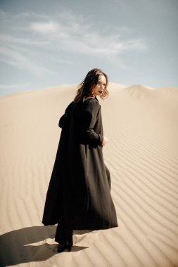 beautiful woman wearing black abaya walking on dune in desert clipart