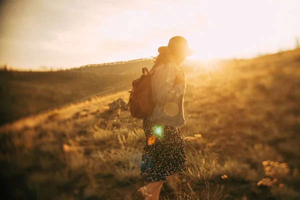 girl with backpack walking on field at sunset