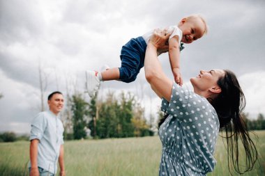 Mutlu genç ebeveynler ve oğullar yaz günü çayırlarda oynarken eğleniyorlar.