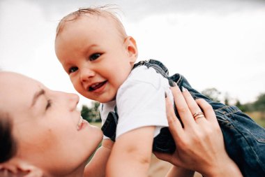 Mutlu, genç bir anne oğlunu elinde tutuyor ve yaz günü çayırda oynarken eğleniyor. 