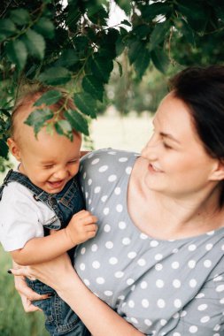 Mutlu, genç bir anne oğlunu elinde tutuyor ve yaz günü çayırda oynarken eğleniyor. 