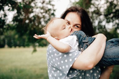 Mutlu, genç bir anne oğlunu elinde tutuyor ve yaz günü çayırda oynarken eğleniyor. 