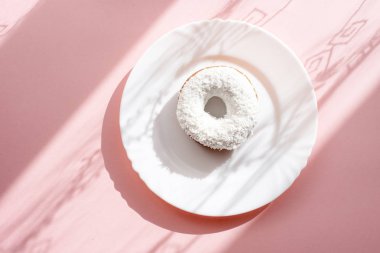 Çörek beyaz sır ile kaplı ve Hindistan cevizi pul gölgeler in numune yüzeyi ile doğal ışık altında pembe bir arka plan üzerinde beyaz bir tabakta serpilir