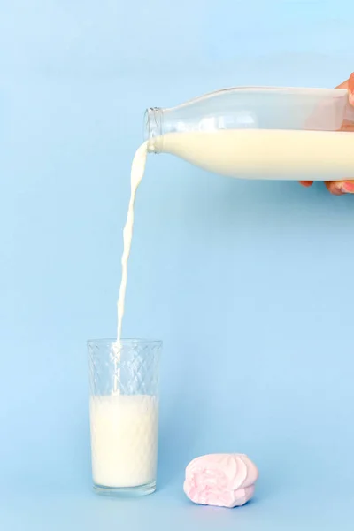 De bouteille en verre transparent versez du lait sur la tasse en verre. Marshmallow près de rose mordu . — Photo