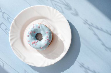 Çörek mavi sır ile kaplı ve doğal ışık altında mavi zemin üzerine beyaz bir plaka üzerinde küçük pembe kalpler serpilir