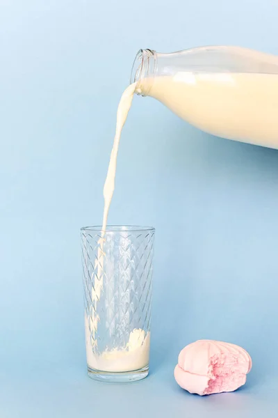 From  transparent glass bottle pour milk on glass Cup. Near pink bitten marshmallow. — Stock Photo, Image