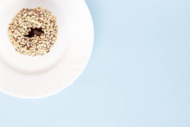 Çörek çikolata sır ile kaplı ve mavi bir masada beyaz tabaklar fındık serpilir