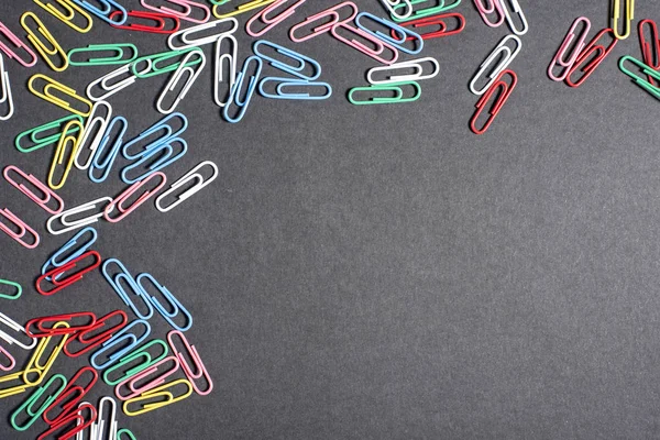 Multi-colored beautiful stationery paper clips on black surface on the top right corner — Stock Photo, Image
