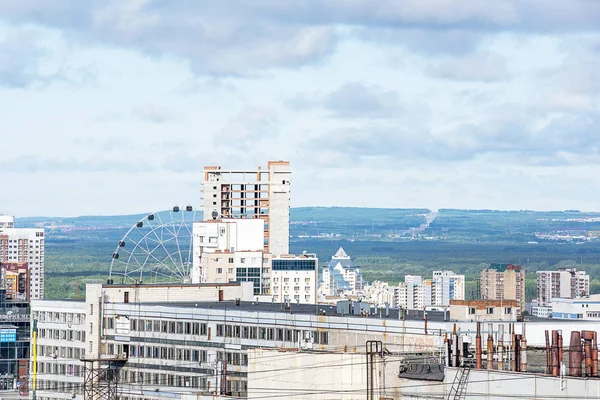 Çok katlı evler ve bir dönme dolap ön planda ve arka planda orman, ufuk