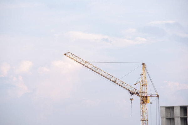 Yellow construction crane on a blue sky background near the multi-storey building
