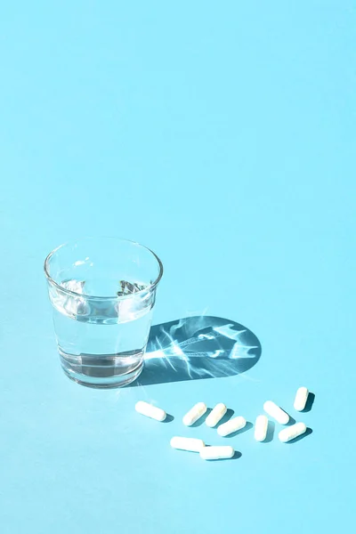 Woda w szklanym pucharze i białe długie kapsułki na powierzchni niebieski — Zdjęcie stockowe