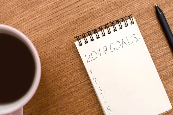 Top view 2019 goals list with notebook, cup of coffee on wooden