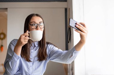 Bir selfie onun elinde bir kafede kahve ile mavi gömlekli koyu saçlı bir kadın lazım