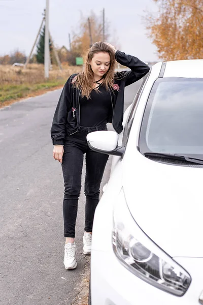 Молодая красивая девушка в черной одежде в осенний день рядом с белой машиной — стоковое фото