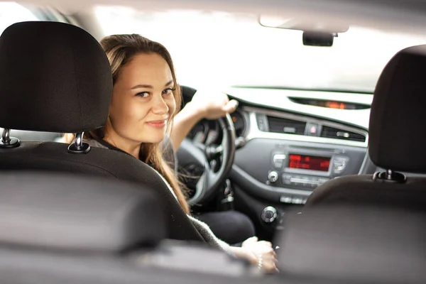 Молодая женщина, сидящая в машине за рулем, оглядываясь назад и улыбаясь — стоковое фото