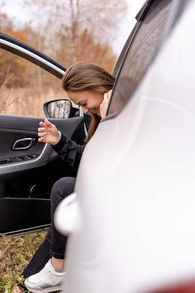 Kaunis nuori tyttö istuu autossa kuljettajan istuimella ovi auki — kuvapankkivalokuva