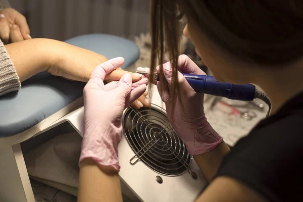 Im Nagelstudio Maniküre-Kundin in rosa Handschuhen entfernt Lack mit Maniküre-Gerät — Stockfoto