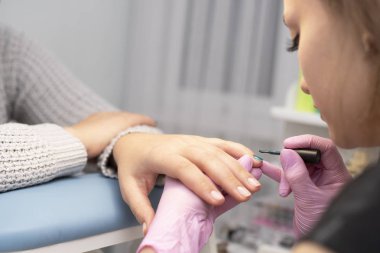 Tırnak salonu bir manikürcü eldiven müşterinin çivi bir fırça ile yeşil oje ile kapsar.