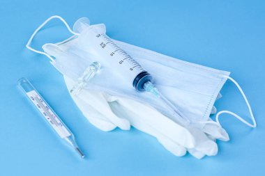 Medical disposable syringe, ampoule, gloves, mask and thermometer on blue background clipart