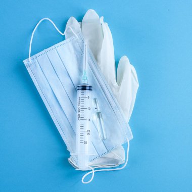 Tıbbi tek kullanımlık şırınga, ampül, eldiven ve maske mavi zemin üzerine .