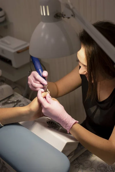 In the nail salon client manicurist in pink gloves removes varnish with manicure device
