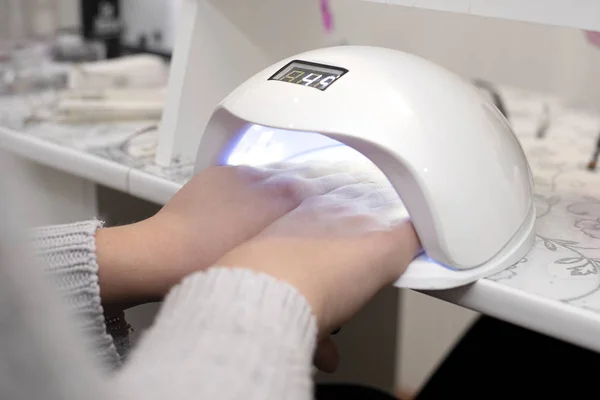 En el salón de uñas mujer seca esmalte de uñas en una lámpara de uñas — Foto de Stock