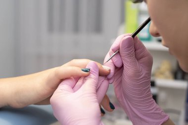 Tırnak salonu bir manikürcü pembe eldiven müşterinin çivi ile tırnak cilası fırça ile kapsar.