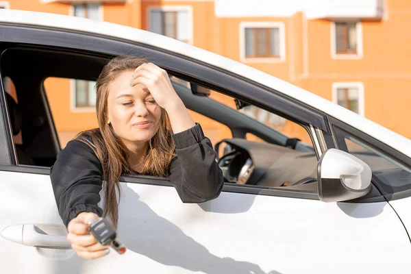 Молодая красивая девушка смотрит из окна машины, в руках у нее ключи от машины, счастливая покупка — стоковое фото