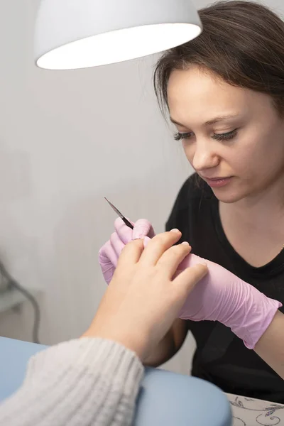 Im Nagelstudio bedeckt eine Maniküre in Handschuhen die Nägel des Kunden mit einem Pinsel mit grünem Nagellack — Stockfoto