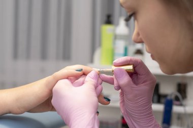 Tırnak salonu bir manikürcü pembe eldiven müşterinin çivi ile tırnak cilası fırça ile kapsar.