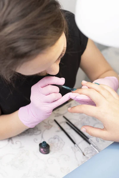 In de nagel salon dekt een manicure in handschoenen van cliënt nagels met een groene nagellak met een borstel — Stockfoto