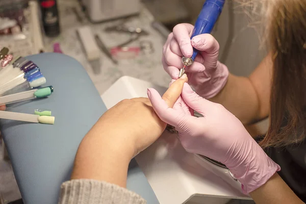 Im Nagelstudio Maniküre-Kundin in rosa Handschuhen entfernt Lack mit Maniküre-Gerät — Stockfoto