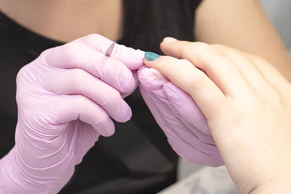 Im Nagelstudio bedeckt eine Maniküre in Handschuhen die Nägel des Kunden mit einem Pinsel mit grünem Nagellack — Stockfoto