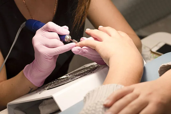 In the nail salon client manicurist in pink gloves removes varnish with manicure device