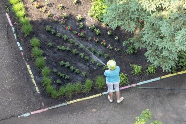 Bilinmeyen bir adam bir hortum ile çiçek Bahçe sulama
