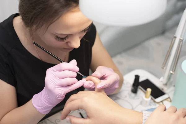 Im Nagelstudio bedeckt eine Maniküre in Handschuhen die Nägel des Kunden mit einem Pinsel mit grünem Nagellack — Stockfoto