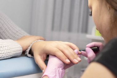 Tırnak salonu bir manikürcü eldiven müşterinin çivi bir fırça ile yeşil oje ile kapsar.