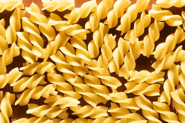 Macarrão na forma de espirais amarelas no fundo marrom — Fotografia de Stock