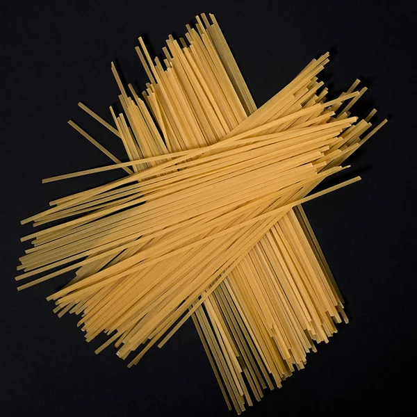 Espaguetis planos crudos sobre fondo negro —  Fotos de Stock