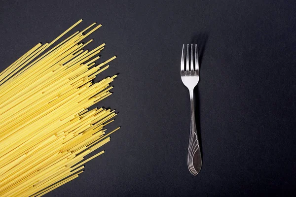 Rohe gelbe Spaghetti und Gabel auf schwarzem Hintergrund — Stockfoto