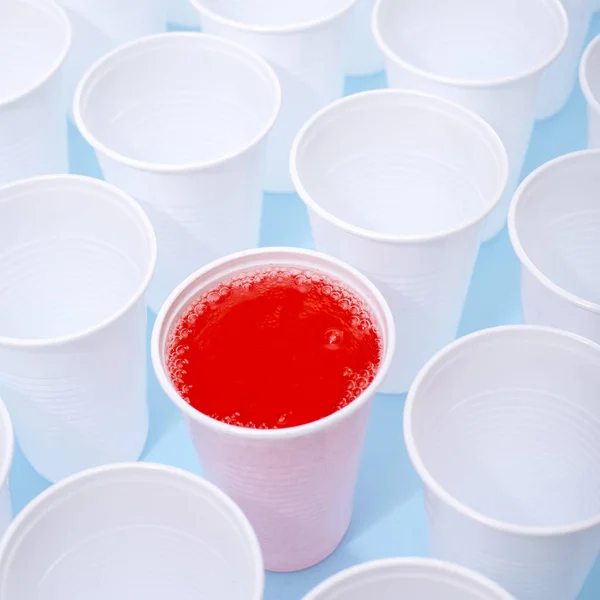 Disposable plastic white empty cups on and one glass filled with red lemonade