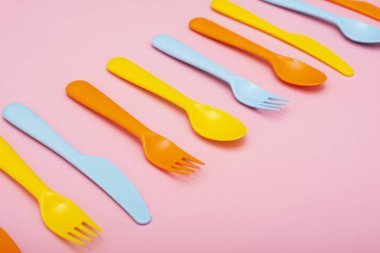 Renkli plastik sofra : çatal, bıçak ve kaşık lar pembe arka plan üzerinde satır